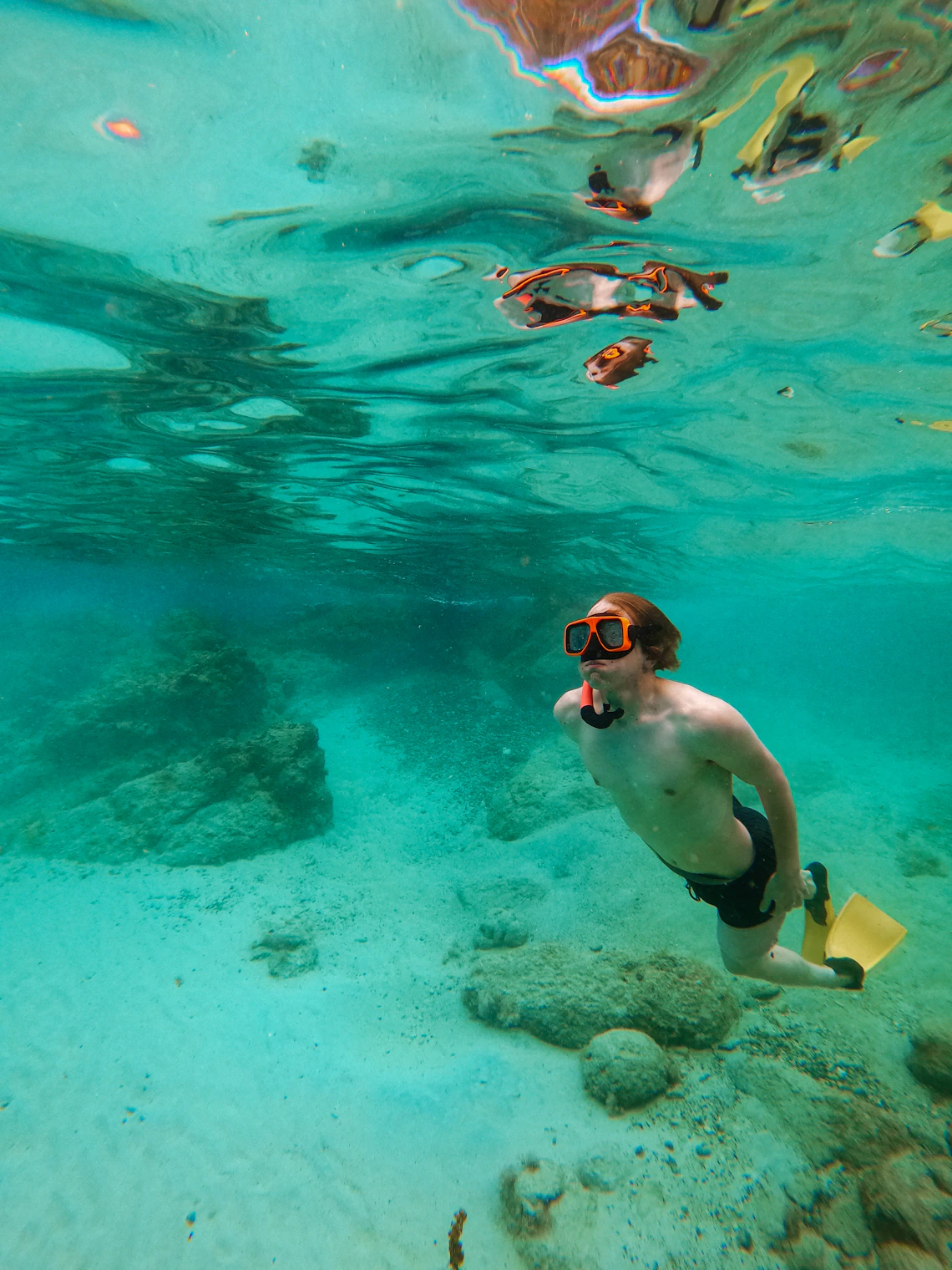 Snorkeler wearing a bright mask exploring crystal-clear turquoise underwater scenery