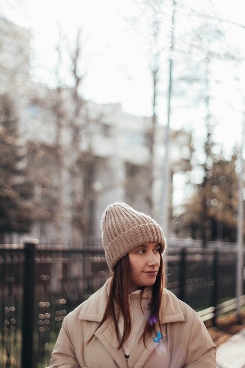 woman in white knit cap and brown coat standing near trees during daytime
