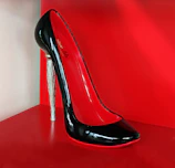 Elegant high-heeled shoe in vibrant red leather displayed on a minimalist wooden surface.