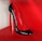 A high-heeled shoe with a glossy black exterior and red interior, featuring a unique silver stiletto heel. The shoe is displayed against a bright red background, highlighting its elegant and sophisticated design.