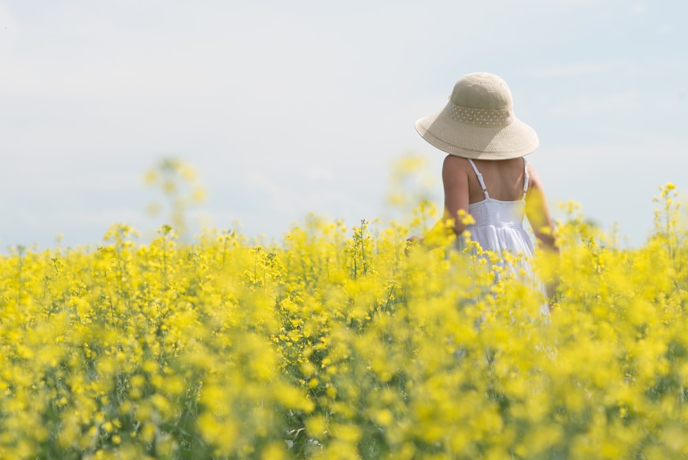 woman in white shirt and brown hat standing on yellow flower field during daytime