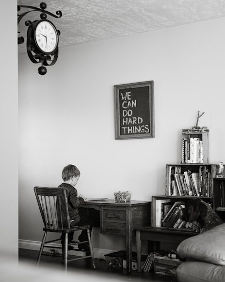 a little boy sitting at a desk under a framed piece of art that reads "We Can Do Hard Things"