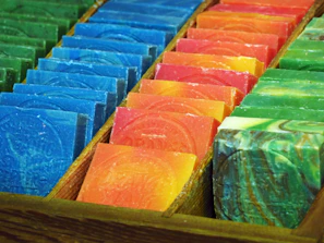 Rows of colorful bar soaps and liquid soaps neatly arranged on wooden shelves.
