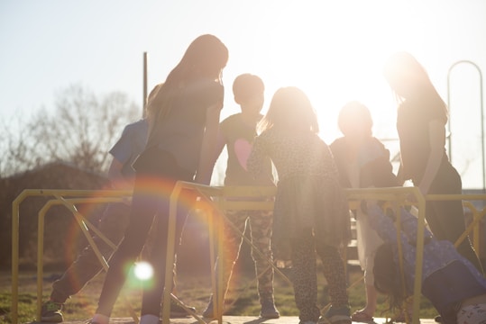 A group of children climbing monkey bars under adult supervision on a sunny day.