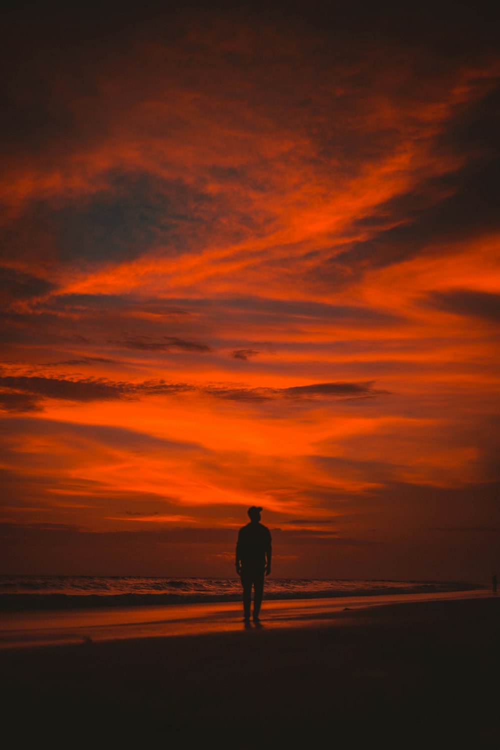 silhueta do homem em pé na praia durante o pôr do sol