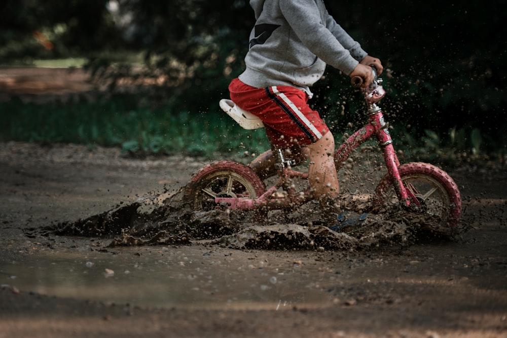 child in gray jacket and red pants riding red bicycle on brown sand during daytime