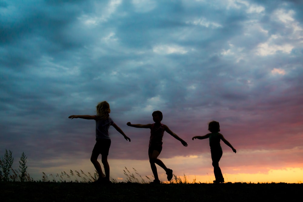 silhouette of 2 women jumping on grass field during sunset