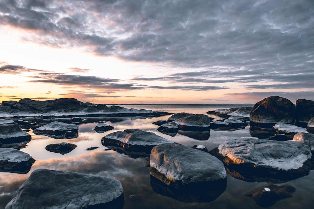 gray and black rocks on body of water under gray clouds