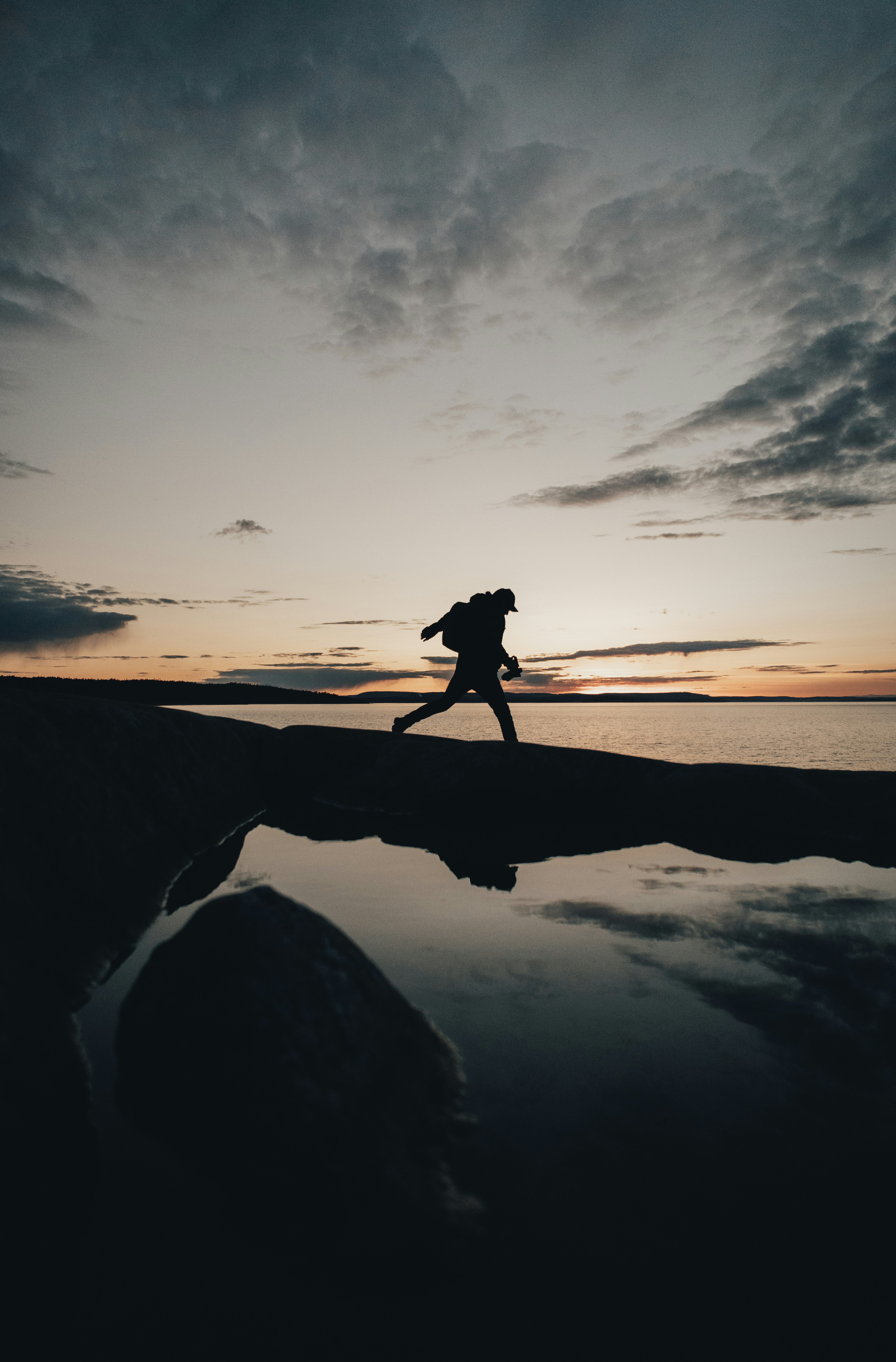 silhouette of woman standing on rock formation near body of water during sunset