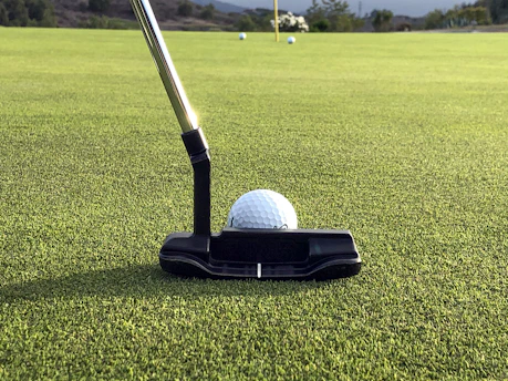 Elegant Ping putter resting on the edge of a golf hole with soft focus on the ball