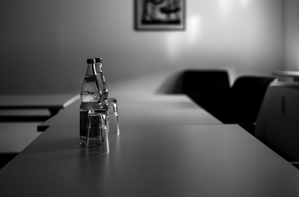 grayscale photo of clear glass bottle on table