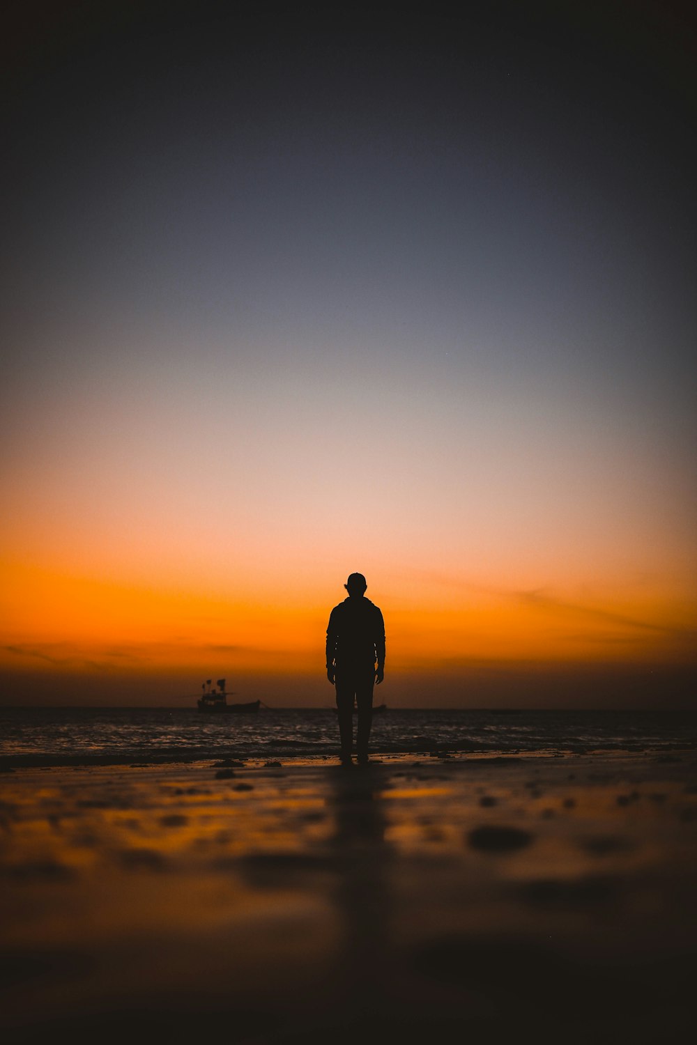 silhueta do homem em pé na praia durante o pôr do sol