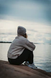 person in gray hoodie and black pants sitting on brown wooden dock during daytime