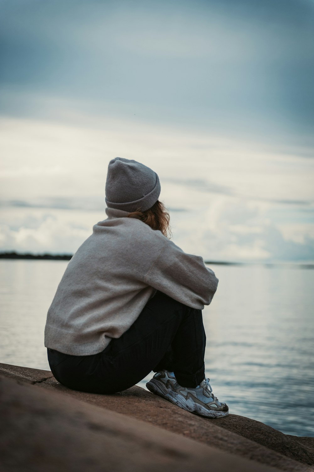 person in gray hoodie and black pants sitting on brown wooden dock during daytime
