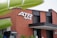A modern building with a red brick facade and large black-framed windows. Prominent signage on the building displays 'ATR Cycling' in bold white letters. There are green leaves partially obscuring the view in the foreground, adding a natural contrast to the architectural scene. Additional smaller signs or structures are visible near the base of the building.