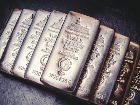 A collection of silver bars from Wall Street Mint, each bar displaying detailed engravings, including the name, weight, and purity of the silver. The bars are arranged in a slight diagonal line and feature a reflective, polished surface.