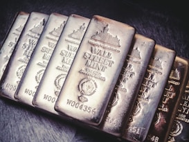 A collection of silver bars from Wall Street Mint, each bar displaying detailed engravings, including the name, weight, and purity of the silver. The bars are arranged in a slight diagonal line and feature a reflective, polished surface.