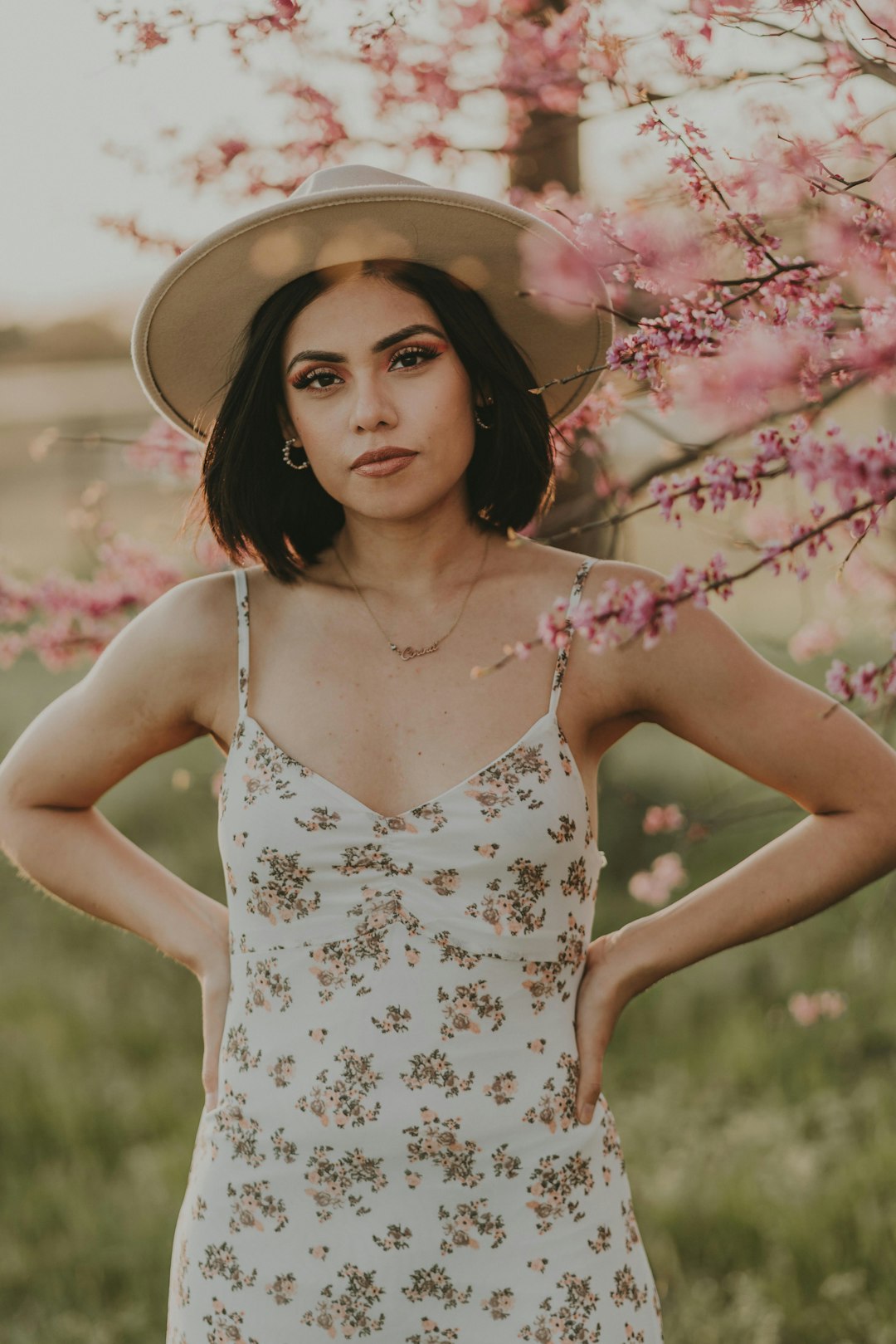 woman in white and blue floral spaghetti strap dress standing beside pink flowers during daytime