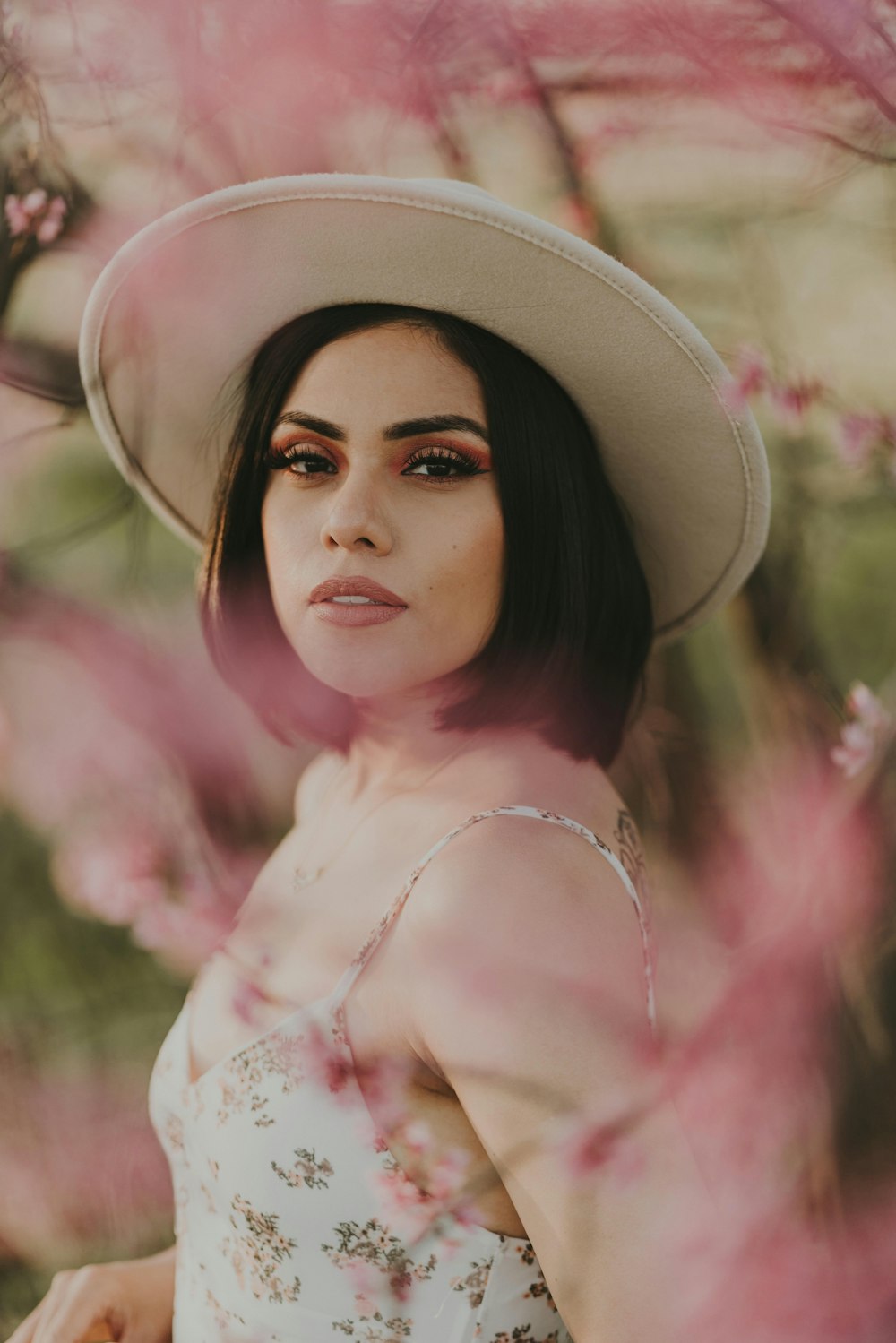 Femme en robe fleurie blanche et rose portant un chapeau marron