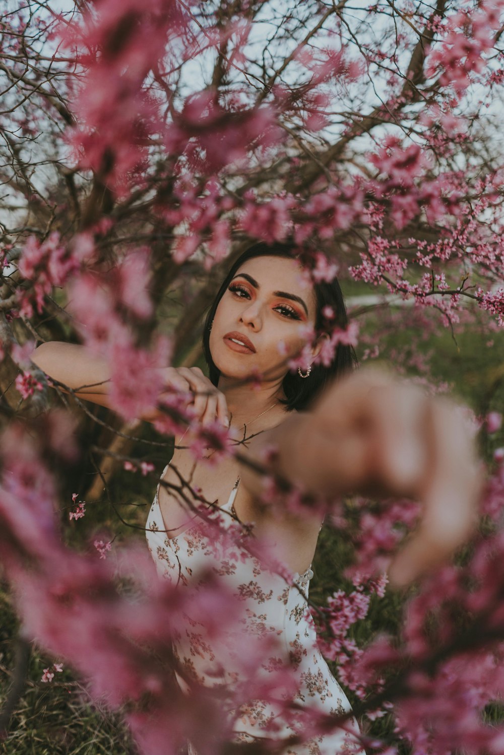 Mujer en vestido floral rosa de pie bajo el cerezo rosa en flor durante el día