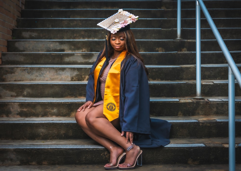 woman in blue and yellow academic dress sitting on stairs