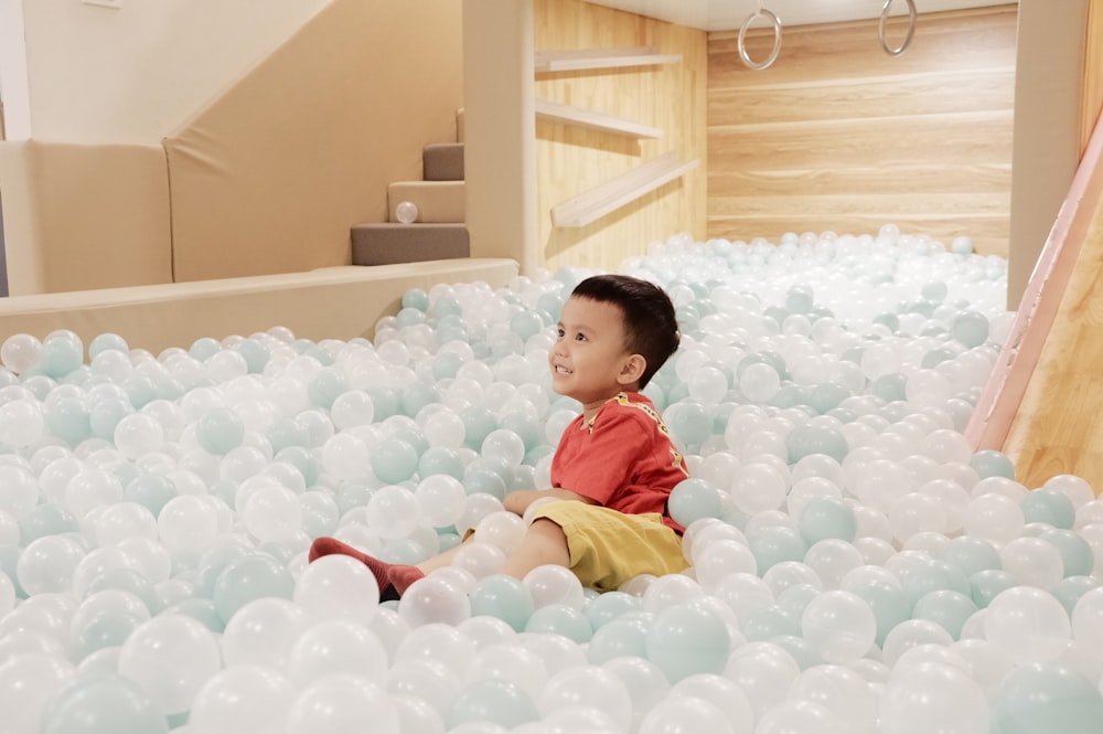 boy in red and yellow polo shirt sitting on white balloons