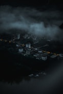 A mist-shrouded village at twilight with faint glowing eyes peering from the darkness.
