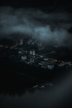 A mist-shrouded village at twilight with faint glowing eyes peering from the darkness.