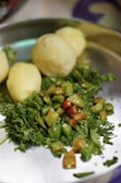 A close-up of a metal plate containing boiled potatoes, chopped green and red chilies, and fresh coriander leaves.