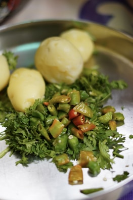 A close-up of a metal plate containing boiled potatoes, chopped green and red chilies, and fresh coriander leaves.