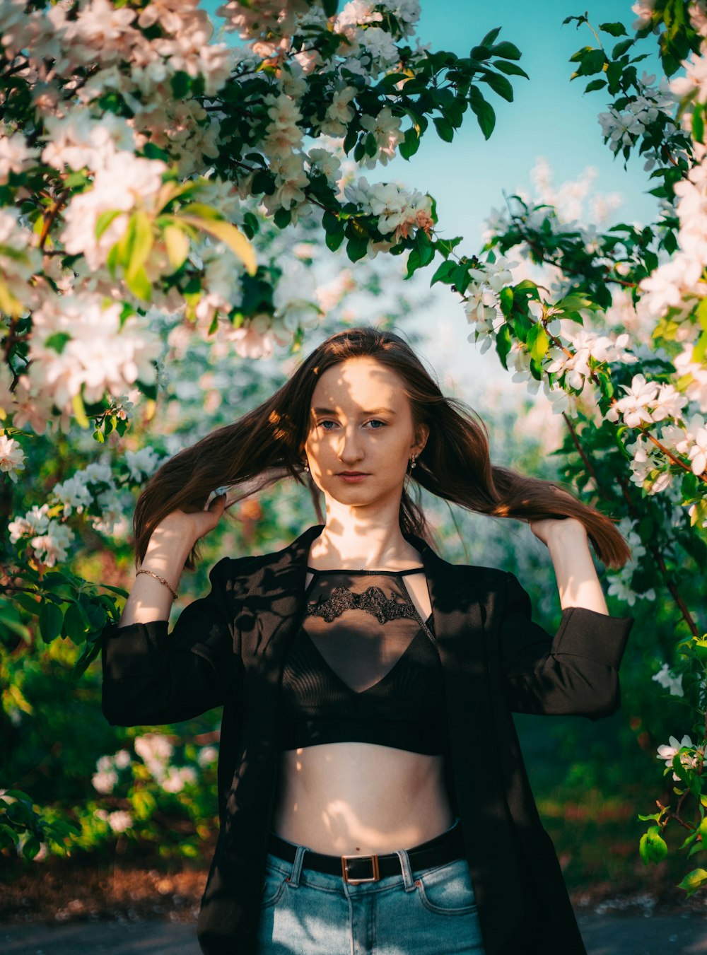 woman in black long sleeved crop top and black brassiere standing under white flower tree during