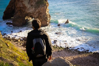 man in black jacket sitting on rock formation near sea during daytime