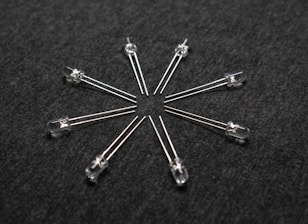 A radial arrangement of several transparent light-emitting diodes (LEDs) with metallic legs extending outward on a dark textured surface.