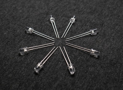 A radial arrangement of several transparent light-emitting diodes (LEDs) with metallic legs extending outward on a dark textured surface.