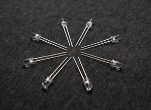 A radial arrangement of several transparent light-emitting diodes (LEDs) with metallic legs extending outward on a dark textured surface.