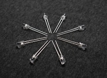 A radial arrangement of several transparent light-emitting diodes (LEDs) with metallic legs extending outward on a dark textured surface.