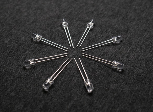 A radial arrangement of several transparent light-emitting diodes (LEDs) with metallic legs extending outward on a dark textured surface.