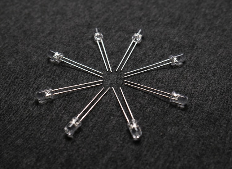 A radial arrangement of several transparent light-emitting diodes (LEDs) with metallic legs extending outward on a dark textured surface.