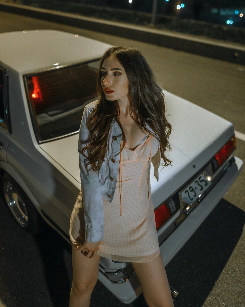 woman in white tank top and orange shorts standing beside white car