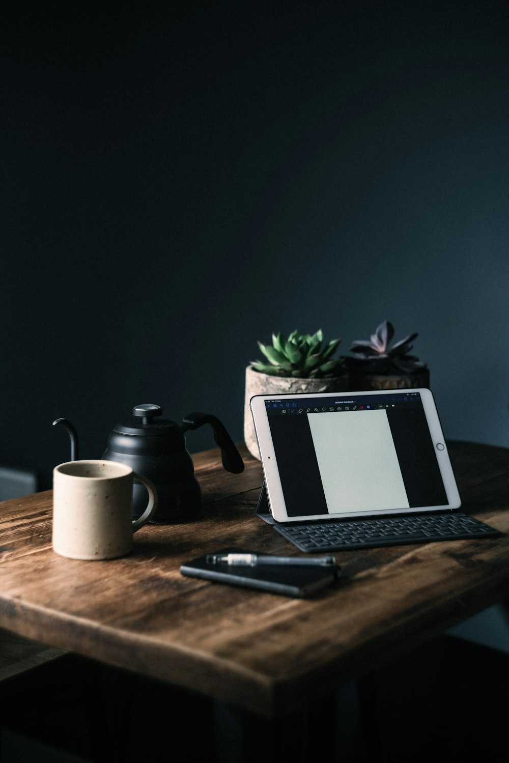 macbook pro beside black click pen and white ceramic mug on brown wooden table