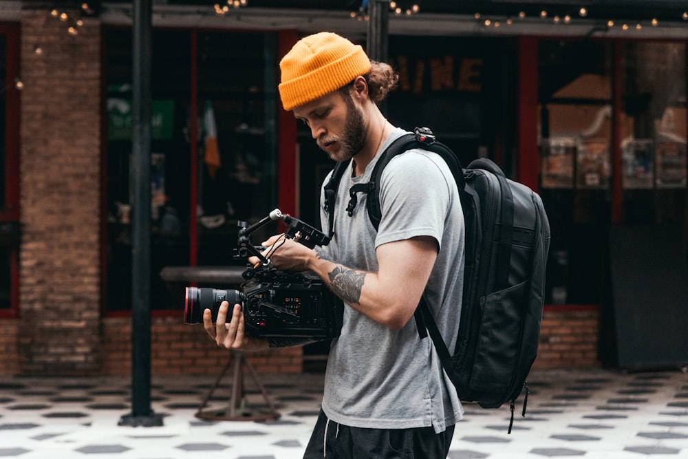 Mann mit grauem Rundhalsausschnitt T-Shirt und gelber Strickmütze mit schwarzer DSLR-Kamera