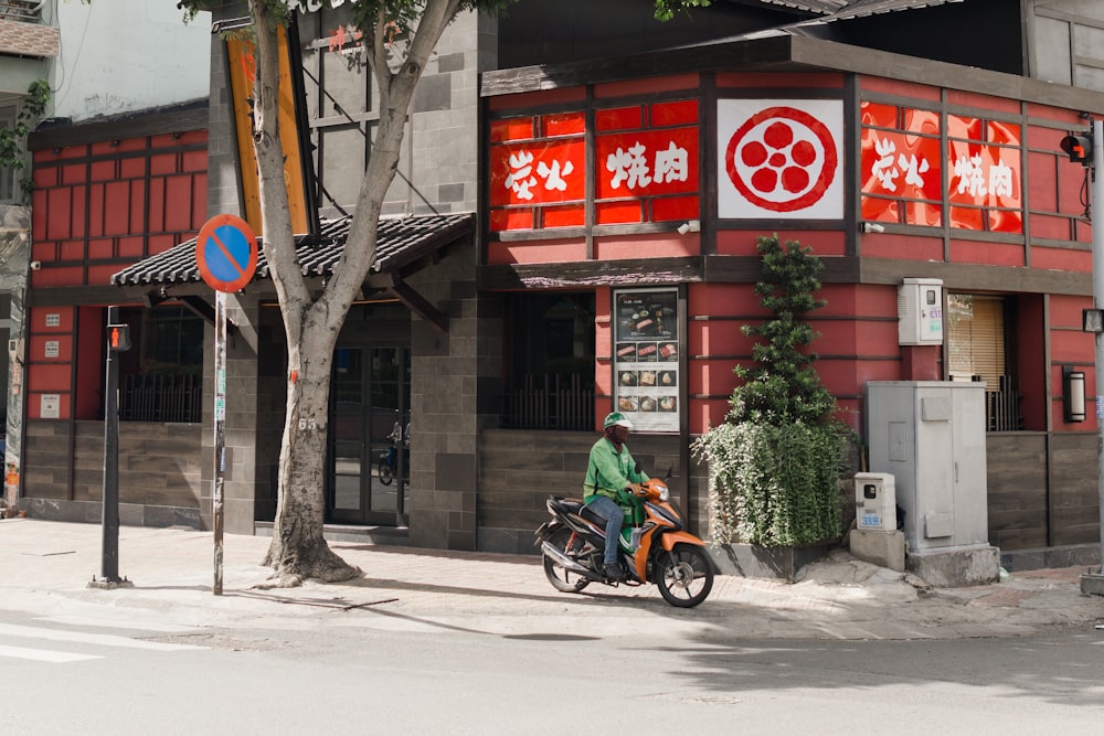 낮 동안 빨간색과 흰색 건물 근처에서 오토바이를 타는 검은 재킷을 입은 남자