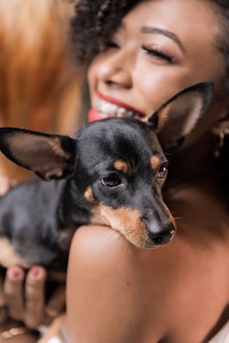 Portrait of a confident woman smiling warmly, with a dachshund by her side.