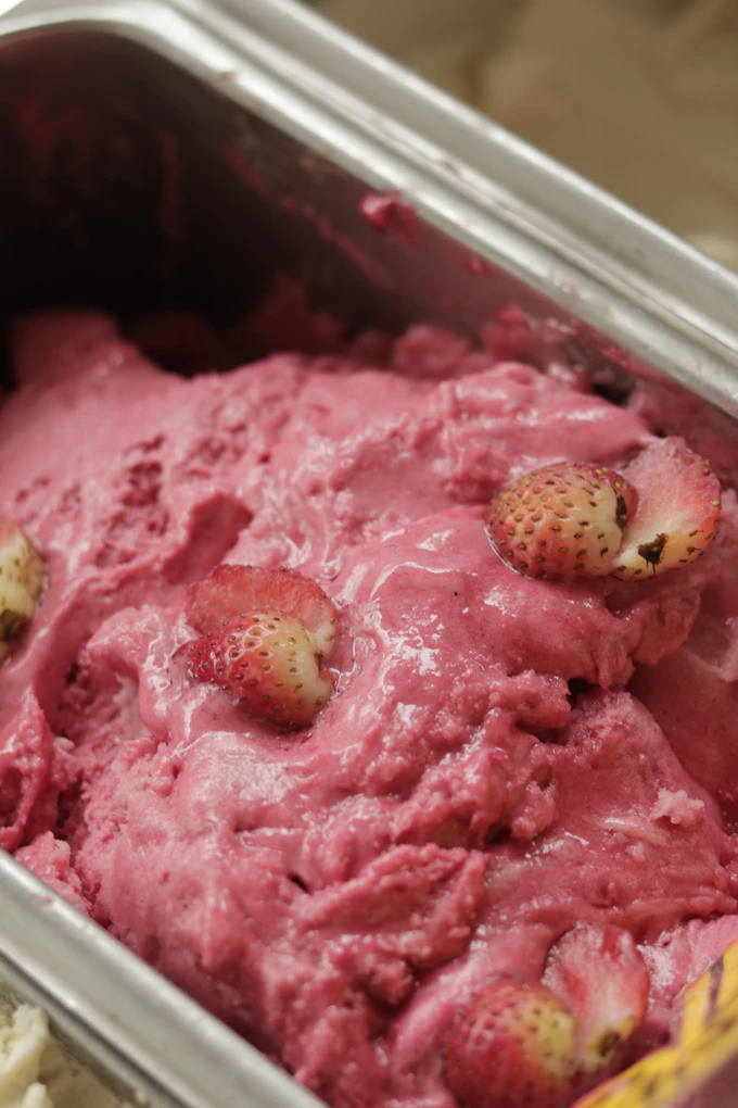 A close-up of fresh strawberries folded into a batch of churning ice cream