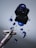 A fountain pen lies on a reflective surface next to an open ink bottle. Blue ink is splattered across the surface, creating a vibrant contrast against the smooth, mirrored background. The pen is elegantly designed, with a delicate floral pattern on its body.