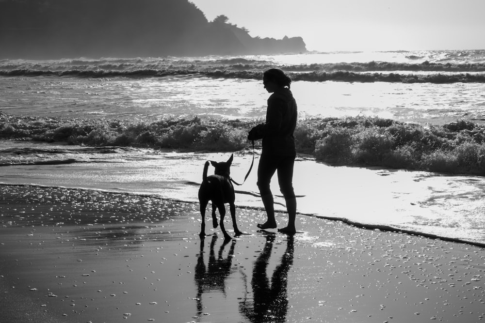 man in black jacket and pants walking with dog on beach shore