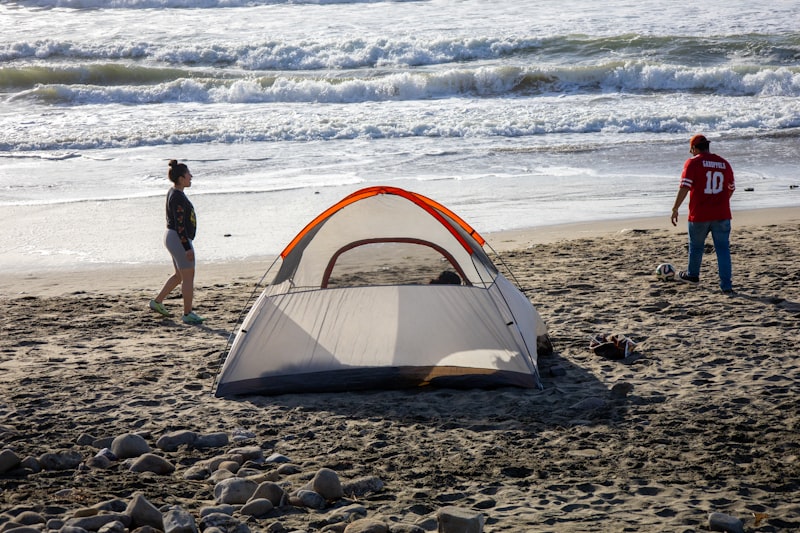 Camping di pantai dengan tenda oranye di tepi laut saat siang hari