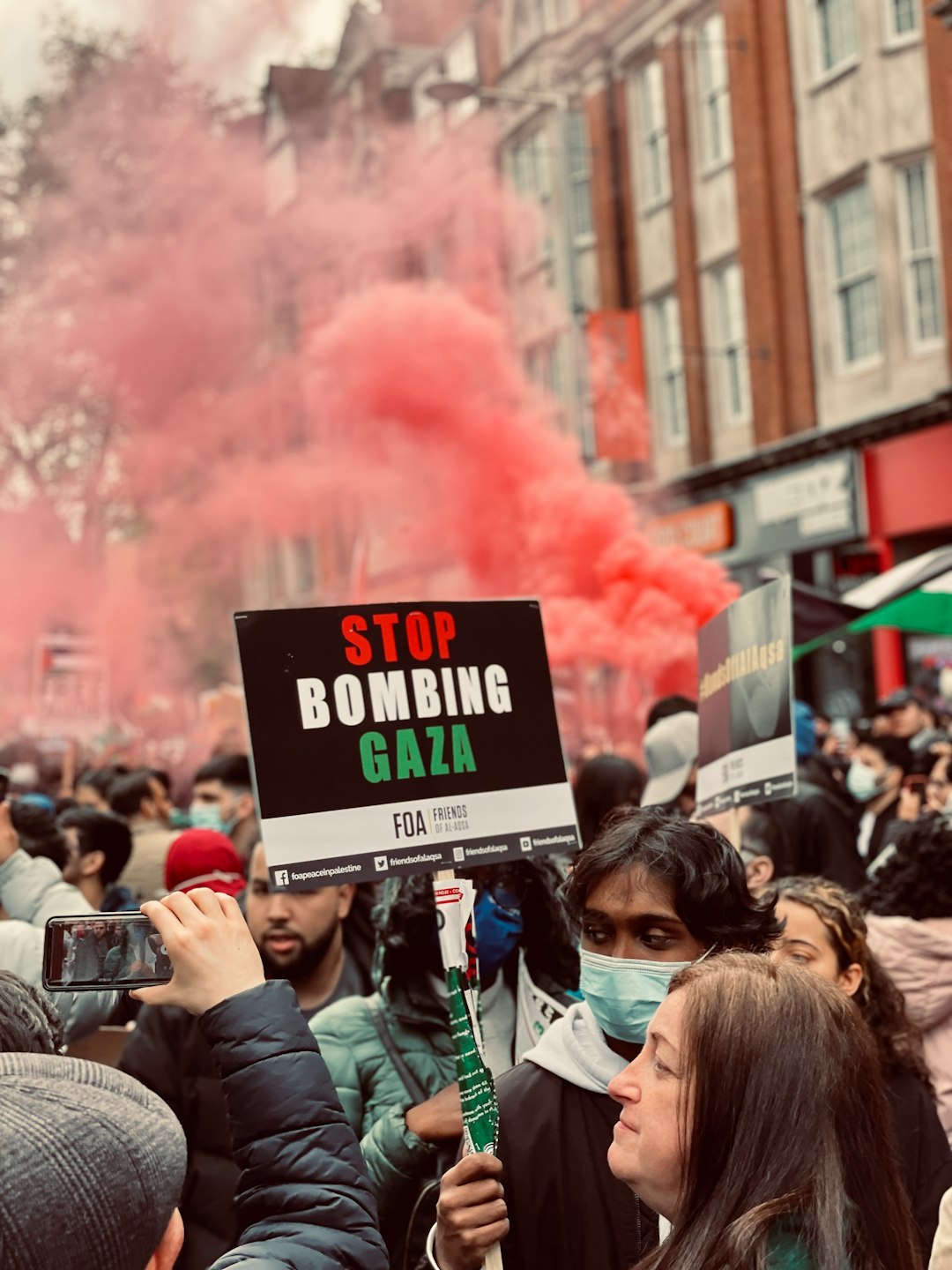 people gathering on street with red smoke during daytime