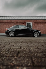 A sleek black and burgundy car being carefully loaded onto a transport truck under a cloudy sky.