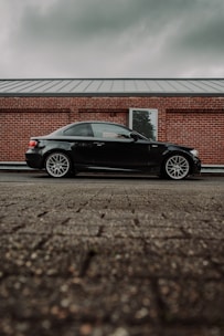 A sleek black and burgundy car being carefully loaded onto a transport truck under a cloudy sky.